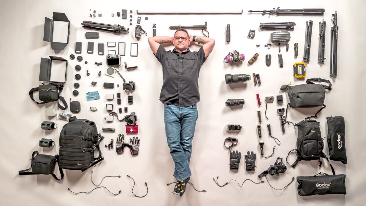 Overhead drone photo of photographer Freaktography lying on the floor surrounded by his full photography gear layout, including cameras, tripods, lenses, and equipment bags.