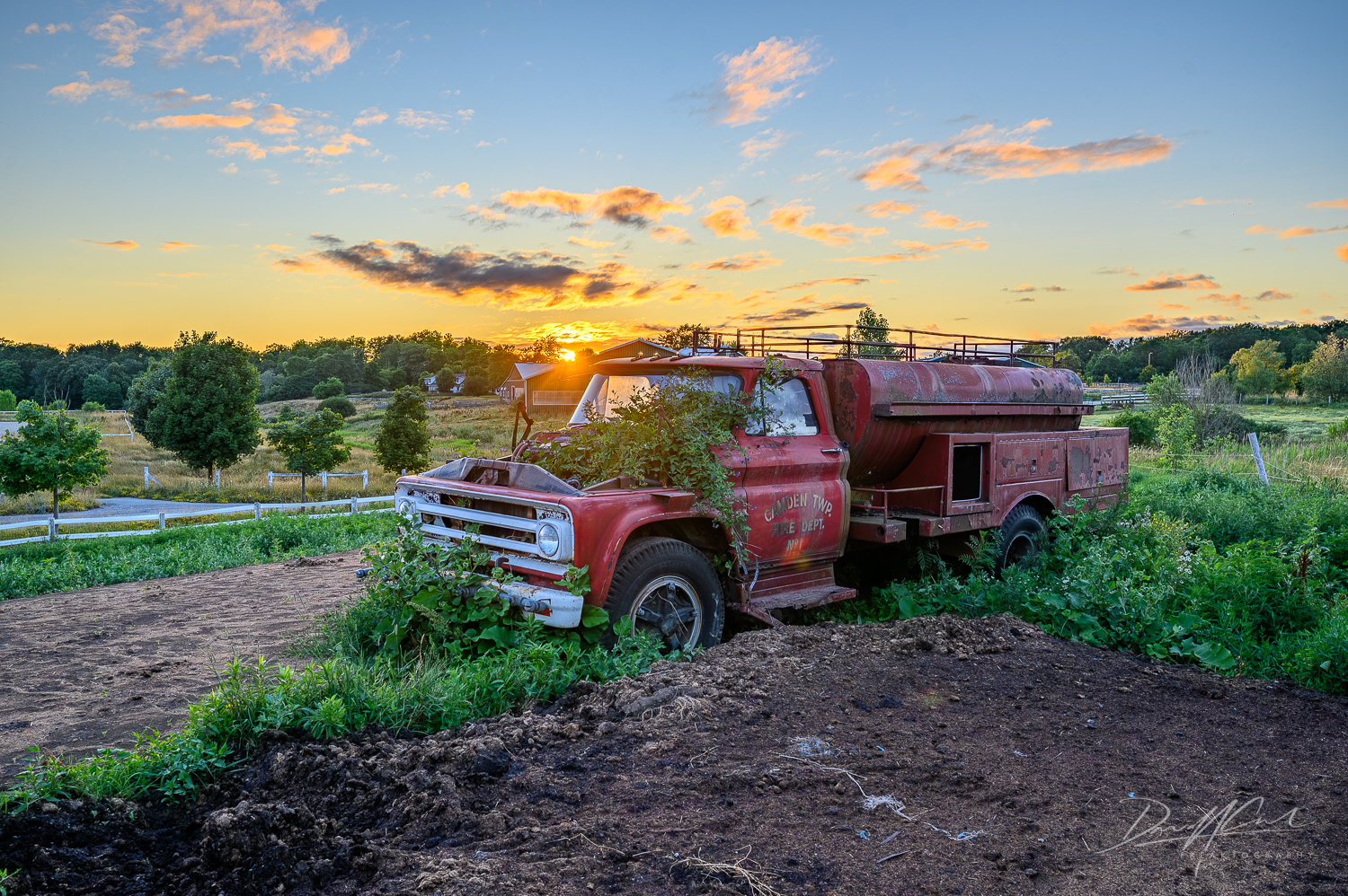 An overgrown fire truck from the Camden Township Fire Department sits quietly on a closed-down farm in rural Ontario as the sun dips below the horizon on a warm July evening.