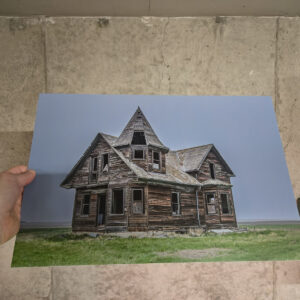 Abandoned two-story Eaton's catalogue house with a turret roof standing in an open prairie field in Saskatchewan.
