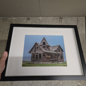 Abandoned two-story Eaton's catalogue house with a turret roof standing in an open prairie field in Saskatchewan.