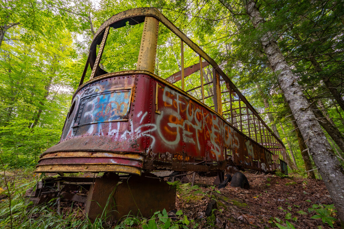 Rusted shell of an old Toronto TTC streetcar abandoned in a forest in Haliburton, Ontario, with trees growing around it.