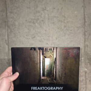 Hardcover Freaktography The Present State of the Past coffee table book with a cover photo of a narrow abandoned hallway leading to a green door.